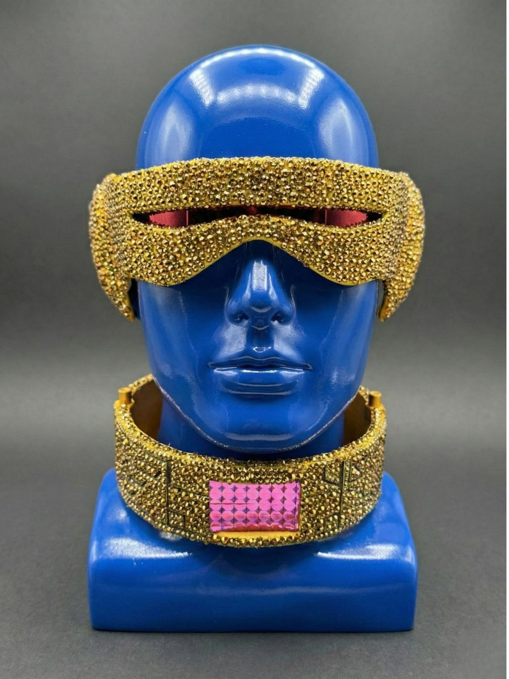 Blue mannequin head with gold and pink decorative accessories on a gray background